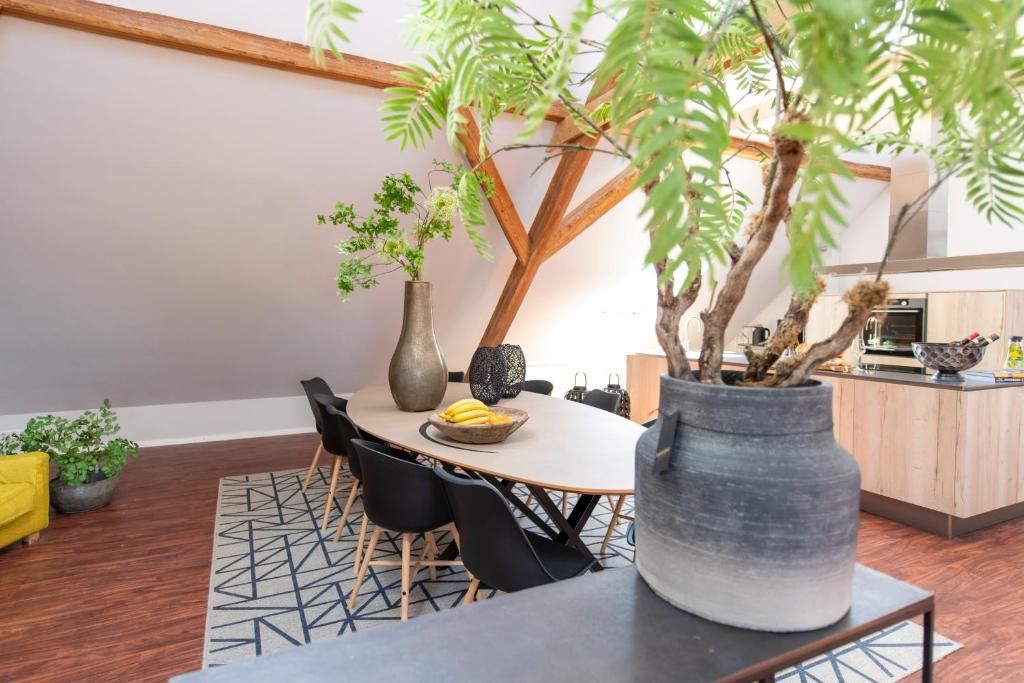 Un coin repas avec une table ronde, des chaises, un vase avec une plante, et une cuisine en arrière-plan.