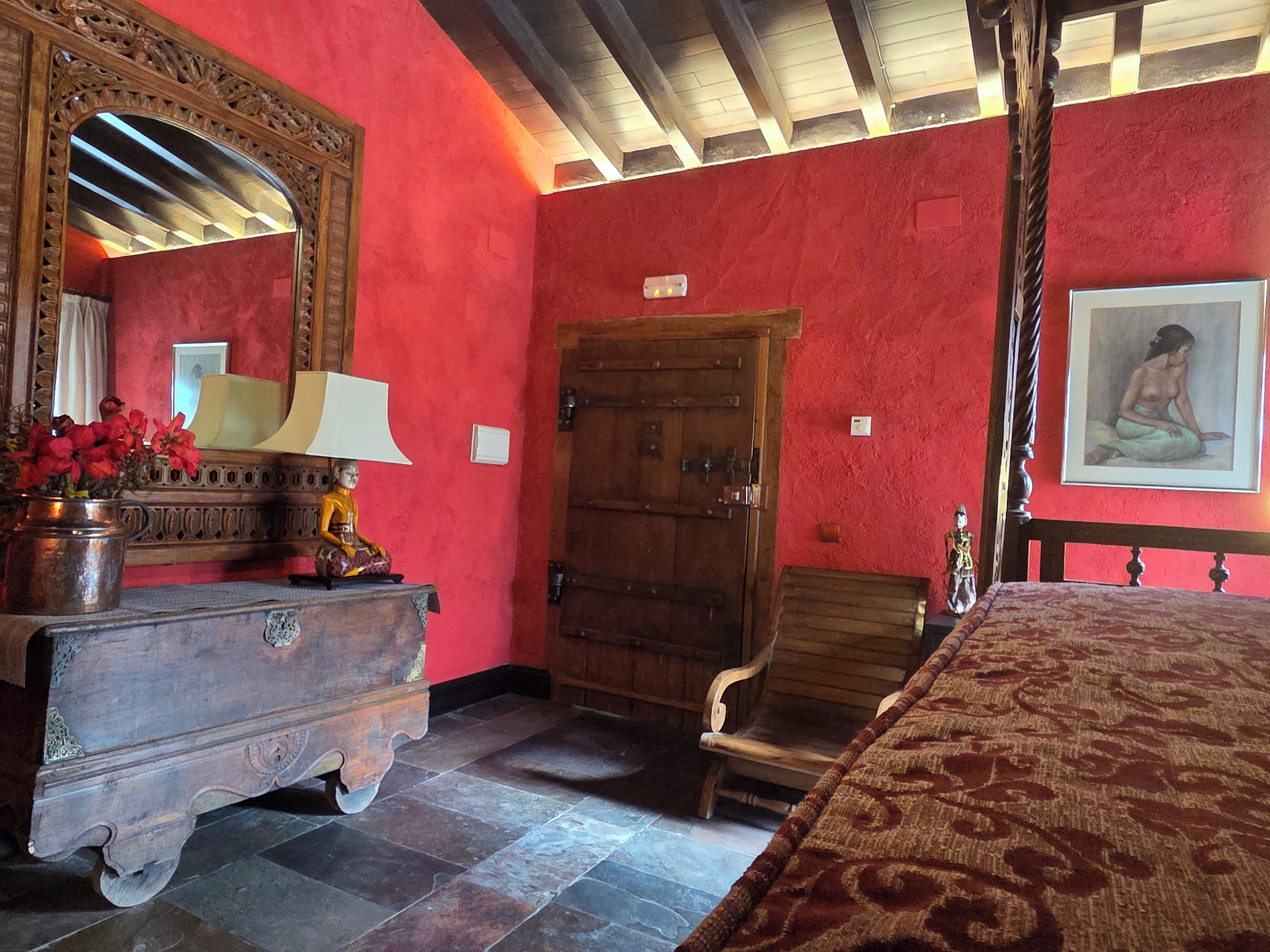 Una habitación con una cama de madera, un tocador con espejo, una puerta de madera y un cuadro en la pared.