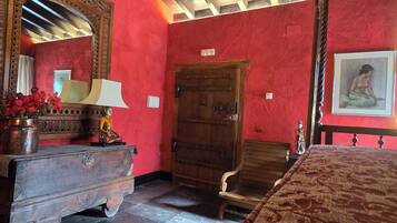 Una habitación con una cama de madera, un tocador con espejo, una puerta de madera y un cuadro en la pared.