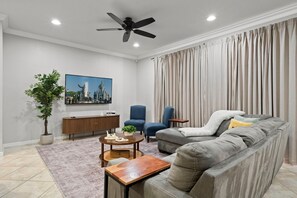 A living room with a sofa, two chairs, a coffee table, a TV, a ceiling fan, and a potted plant. - 5BR townhome near Disney | Pool, by clubhouse (Kissimmee)
