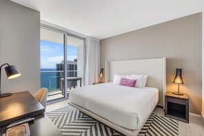 A hotel room with a large bed, a desk, a chair, a TV, and a view of the ocean. - Oasis 2 BR Pool & Views for 6 (Hollywood)