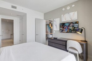 Quarto moderno com uma cama grande, uma escrivaninha com cadeira e televisão na parede exibindo pôsteres de filmes.