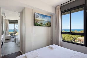 A hotel room with a bed, a painting, a large window with a view, and a balcony with a chair. - Stunning Coastal Escape with Private Balcony (Nahariya)