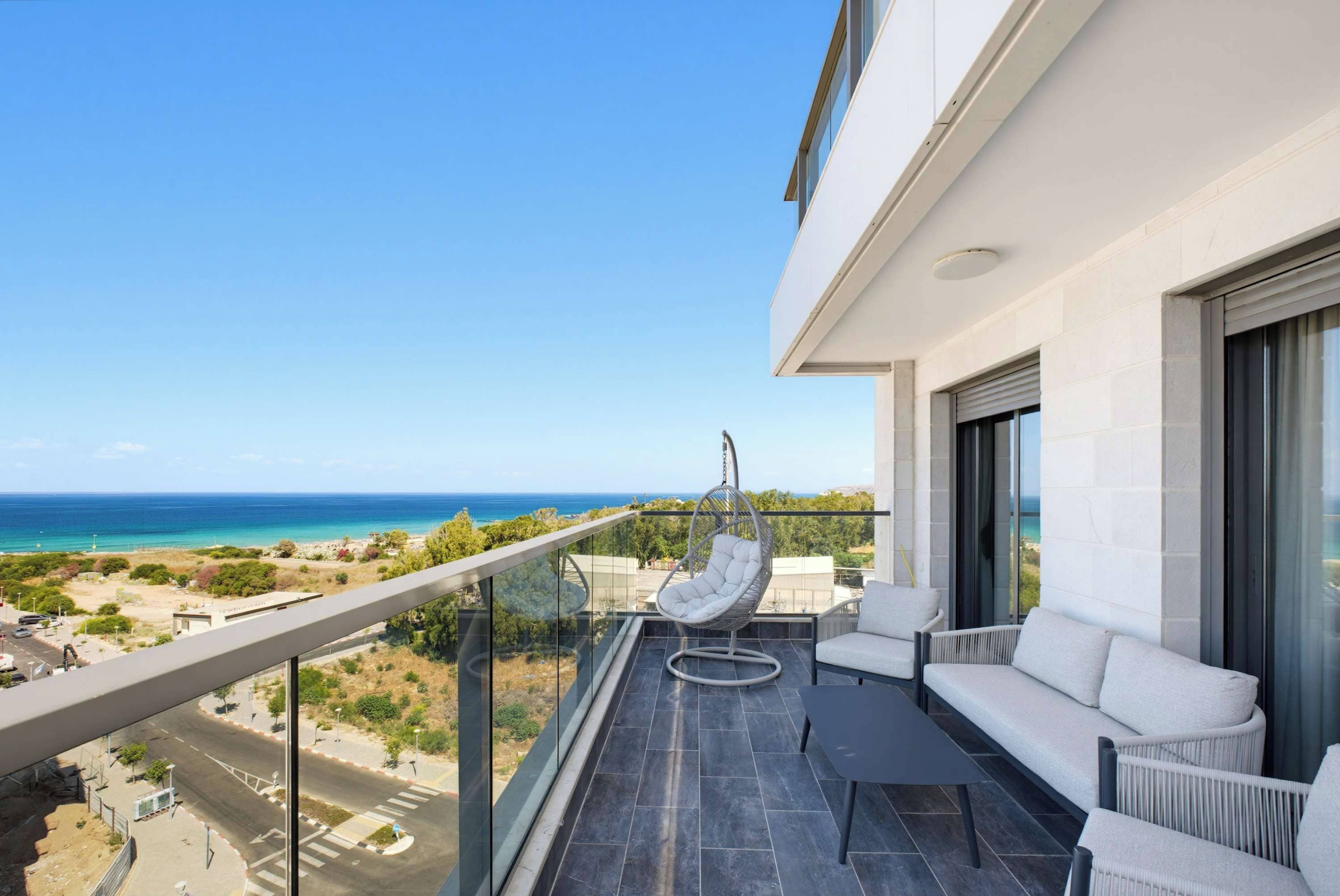 A balcony with a hanging chair, a sofa, and a view of the sea.