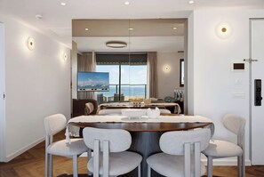 A modern dining area with a round table, four chairs, and a view of the sea through large windows. - Stunning Coastal Escape with Private Balcony (Nahariya)