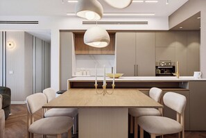 Una cocina moderna con una isla central, iluminación colgante y un comedor con sillas.