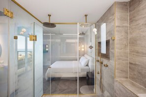 Ein modernes Badezimmer mit Glasabtrennung, Duschbereich und einem Bett mit weißer Bettwäsche.