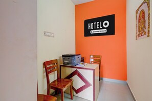 Habitación de hotel con escritorio, dos sillas, impresora y un letrero que indica que el servicio de la habitación es proporcionado por la empresa.