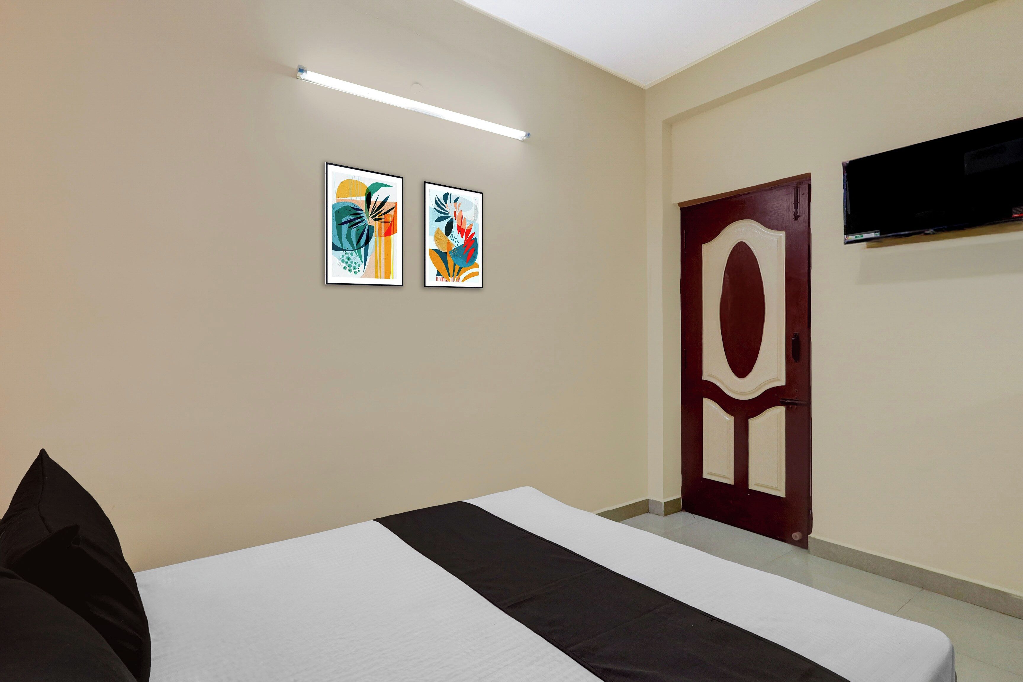 Habitación de hotel con cama, dos cuadros en la pared, un televisor sobre la puerta y una lámpara en el techo.