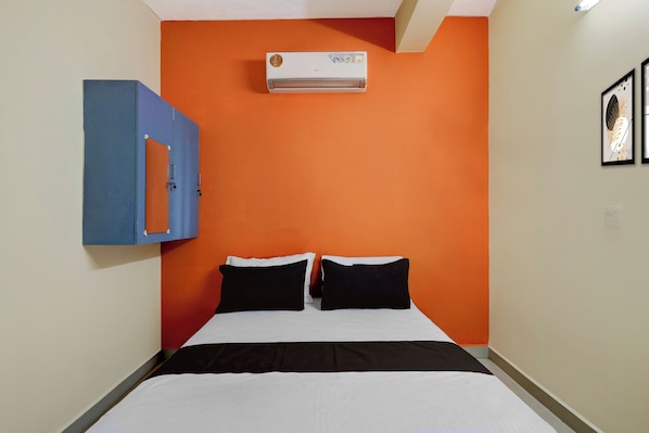 Una habitación de hotel con cama, armario azul, equipo de aire acondicionado y dos cuadros en la pared.