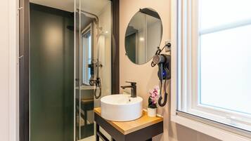 A bathroom with a white sink, a round mirror, a handheld showerhead, and a window with blinds.