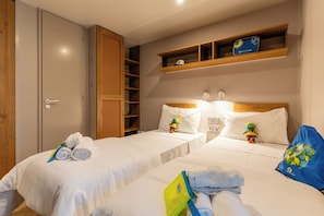 A hotel room with two beds, a wardrobe, a shelf with a pet bed, and a wall-mounted light. - Club del Sole Laguna Boutique Resort (Riccione)