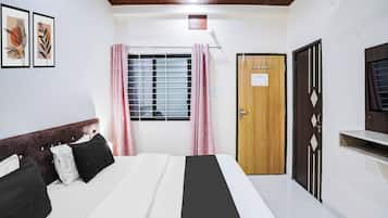 Ein Hotelzimmer mit Bett, Fenster mit Vorhängen, einer Tür und einem an der Wand befestigten Fernseher.