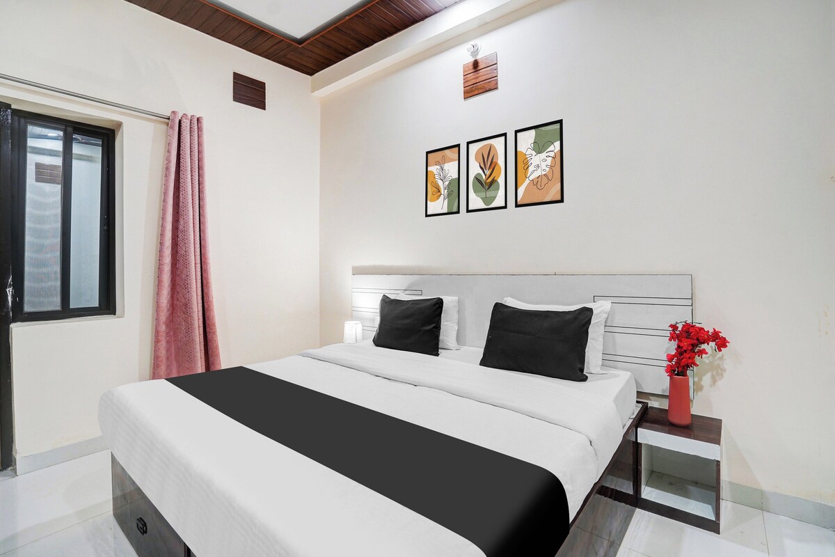 A hotel room with a bed, a nightstand, a window with curtains, and wall art.