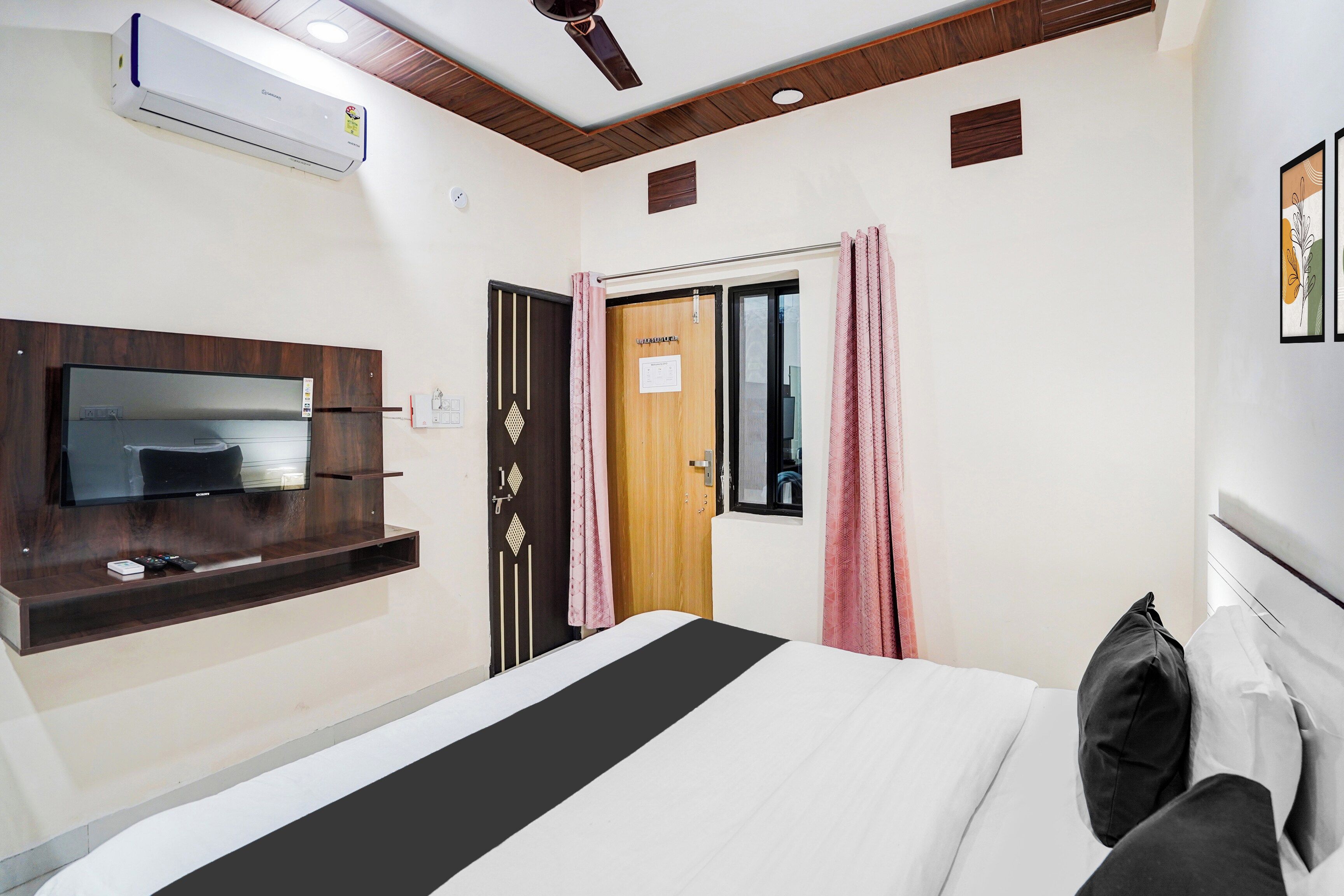 A hotel room with a bed, a TV mounted on the wall, a ceiling fan, and an air conditioning unit.