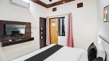 A hotel room with a bed, a TV mounted on the wall, a ceiling fan, and an air conditioning unit.