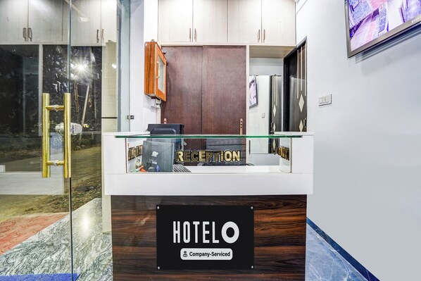 Una recepción de hotel con un separador de vidrio, mostrador de madera y un cartel que indica servicio de empresa.