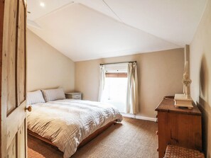 Ein Schlafzimmer mit einem Bett, einem Nachttisch, einer hölzernen Kommode und einem Fenster mit Vorhängen.