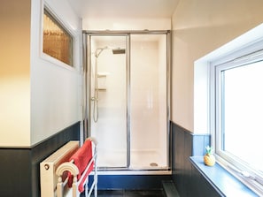 Ein Badezimmer mit einer gläsernen Duschkabine, einem Handtuchhalter mit einem roten Handtuch und einem Fenster mit einer Ananas-Dekoration.