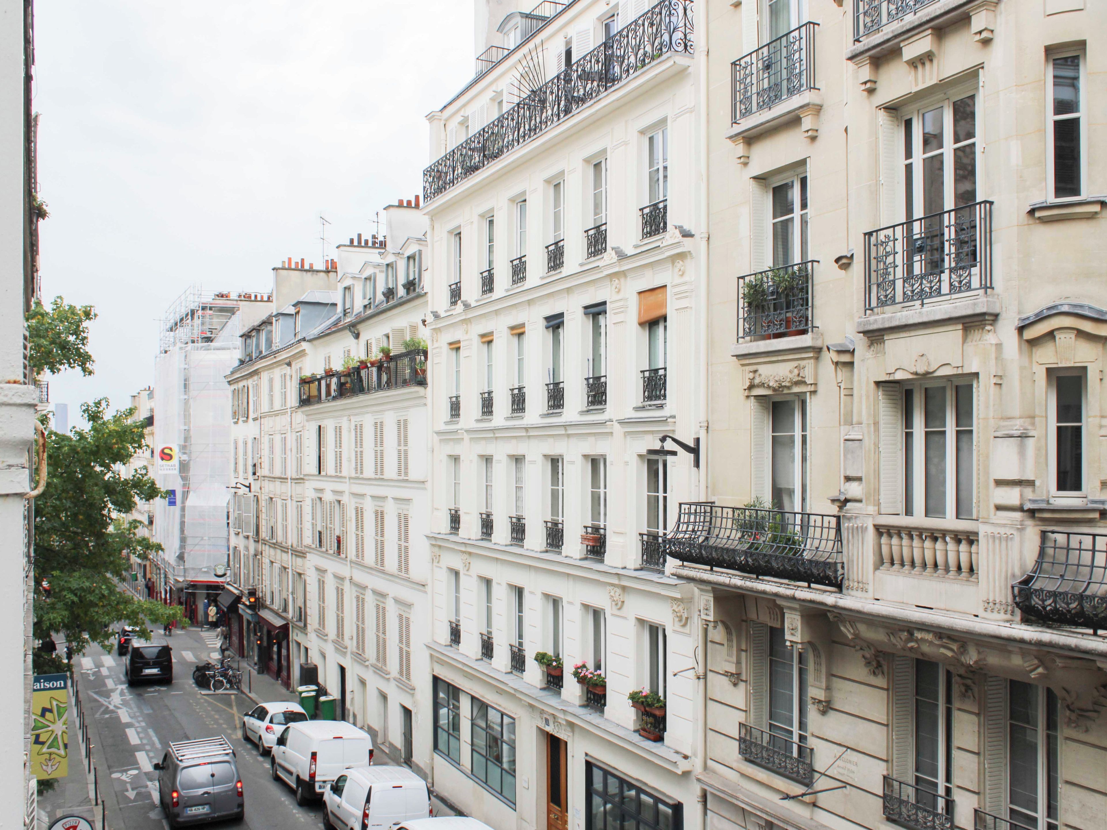 A row of white buildings with balconies, parked cars, and a clear sky.