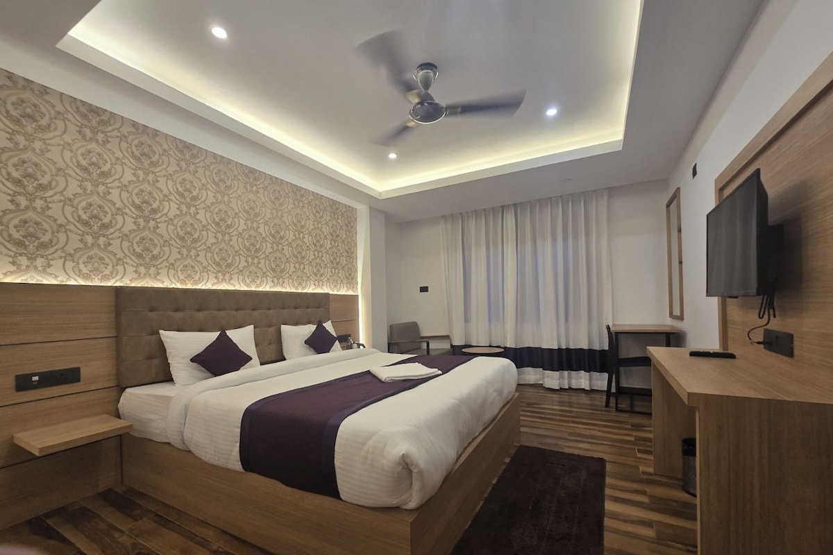 A modern hotel room with a large bed, a desk, a television, and a ceiling fan.