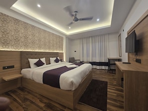 Una habitación de hotel moderna con una cama grande, un escritorio, un televisor y un ventilador de techo.