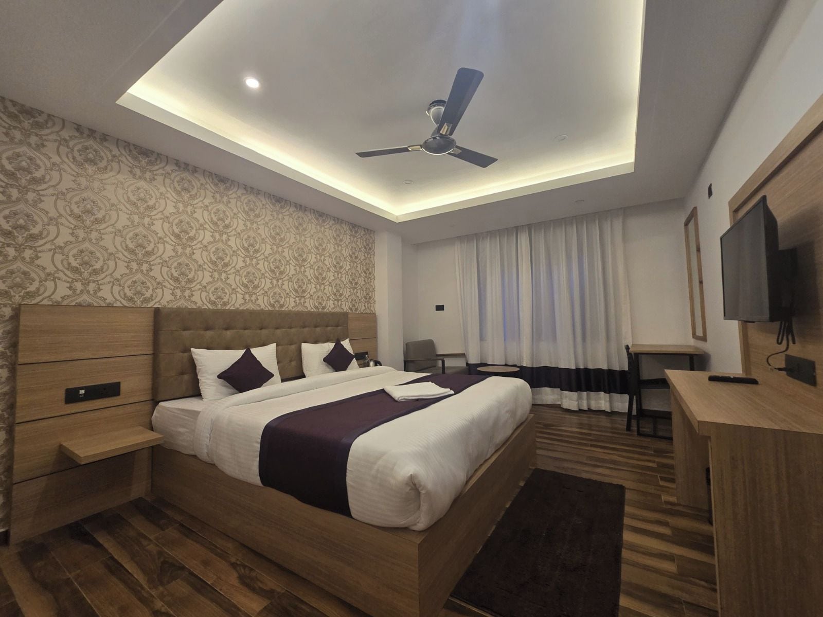 Una habitación de hotel moderna con cama, escritorio, ventilador de techo y televisión.