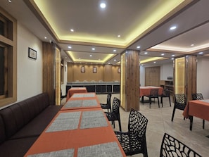 Un restaurante con una larga mesa común, mesas individuales y una zona de estar con sofás.