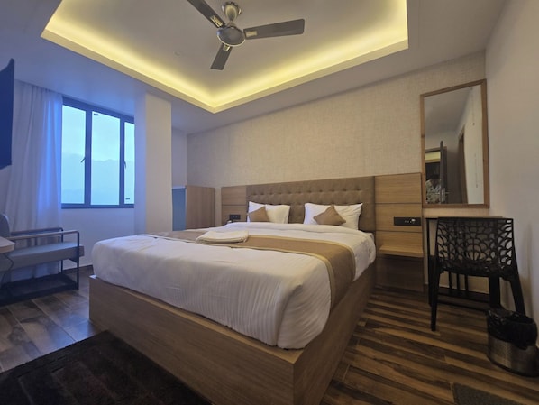 Habitación de hotel con cama, escritorio, silla, ventilador de techo y una ventana grande.