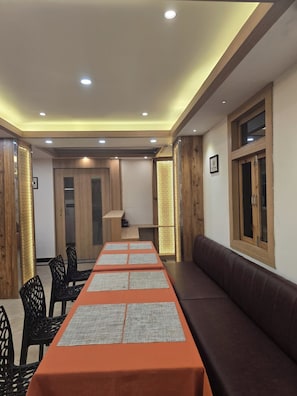 Un salón de conferencias con una larga mesa, sillas negras, un sofá marrón, detalles de madera e iluminación empotrada en el techo.