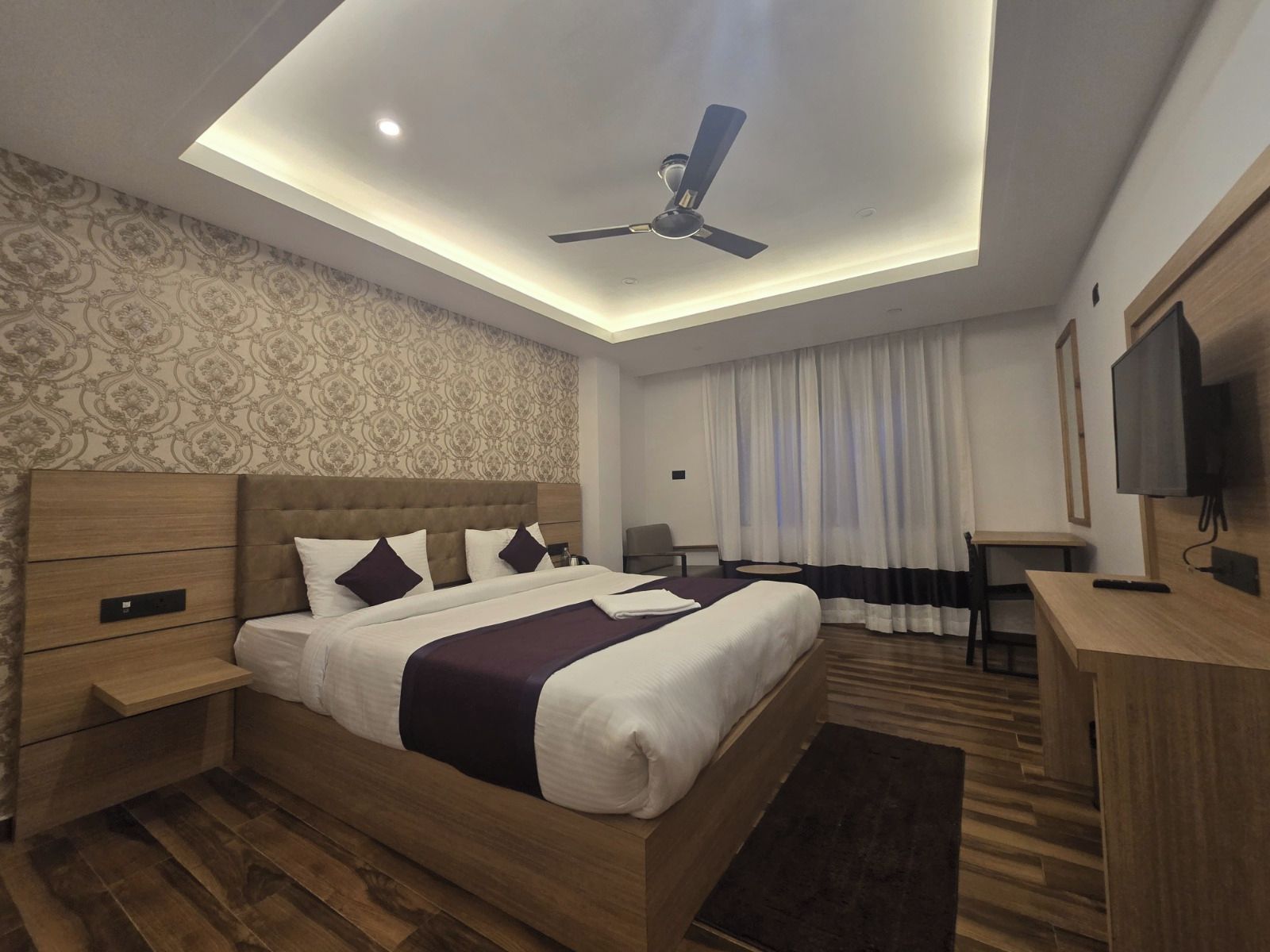 Une chambre d’hôtel moderne équipée d’un lit, d’un bureau, d’un ventilateur de plafond et d’une télévision.