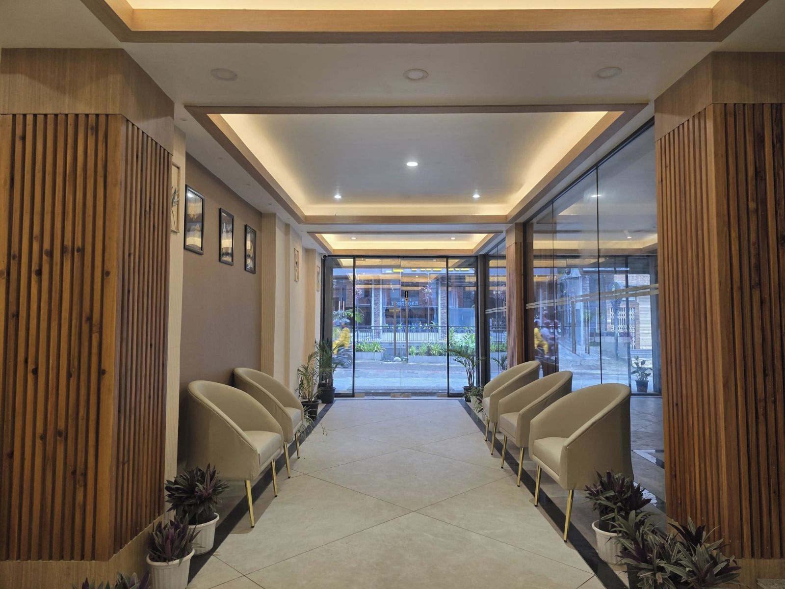 Un espace d’accueil au design moderne, comprenant un espace de repos central avec des fauteuils et des plantes en pot, ainsi qu’une porte vitrée donnant sur l’extérieur.