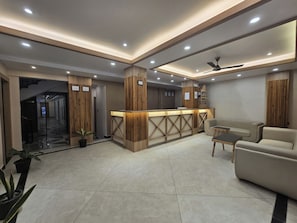 Un área de recepción moderna con un mostrador de madera, zona de estar y un ventilador de techo.