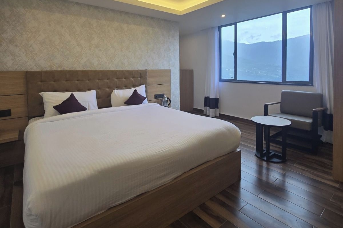 A modern hotel room with a large bed, a seating area, and a view of the mountains.