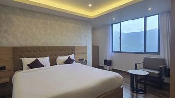 A modern hotel room with a large bed, a seating area, and a view of the mountains.