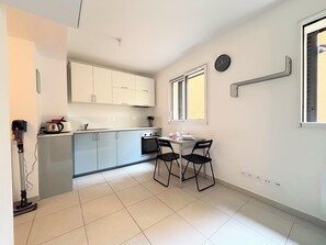 A compact kitchen with white cabinets, a dining table with two chairs, a built-in oven, and a window with blinds. - Convenient studio with Wi-Fi near Nice city centre (Nice)