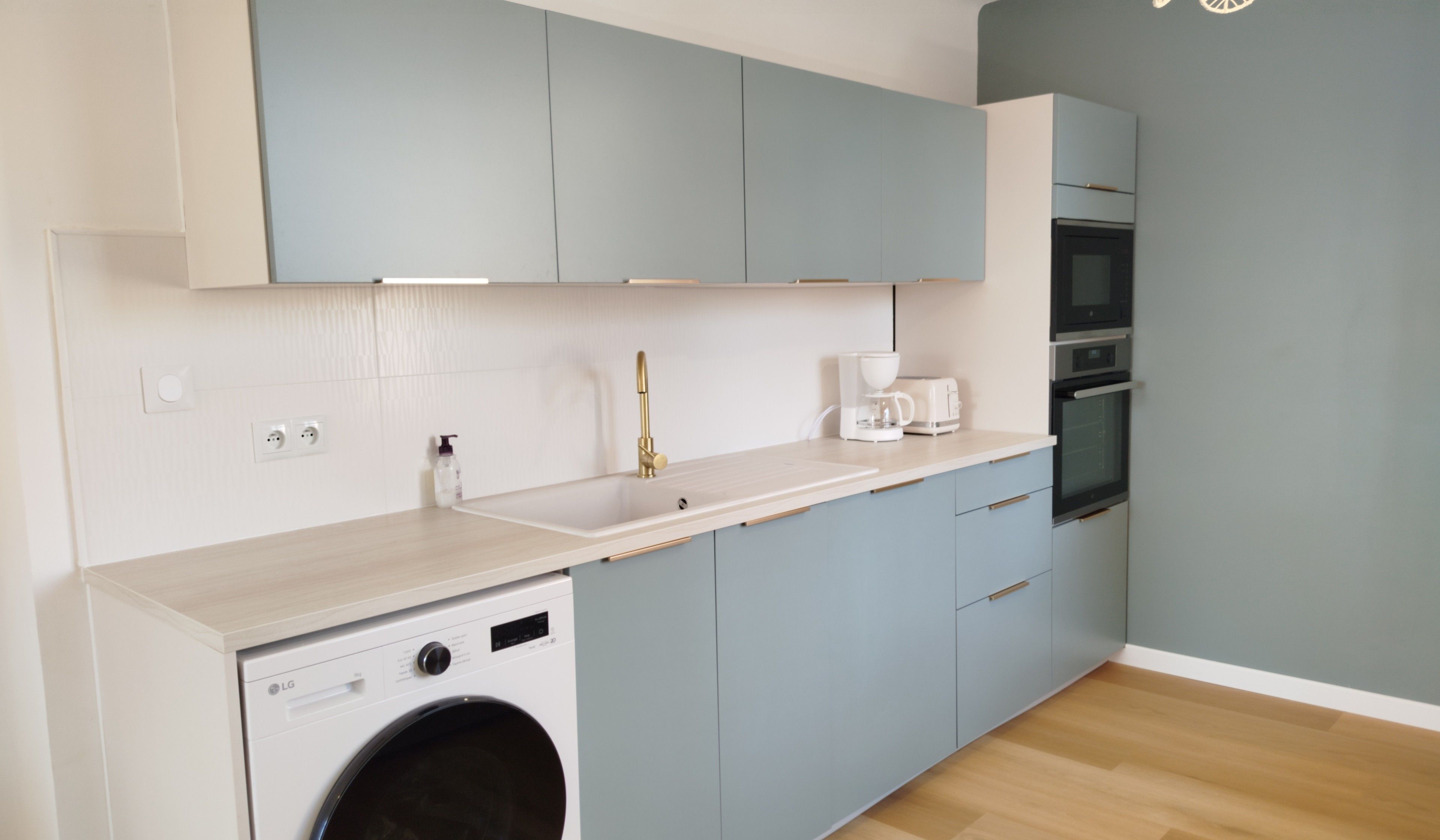 Een kleine keuken met een wasmachine, een spoelbak en een koffiezetapparaat.