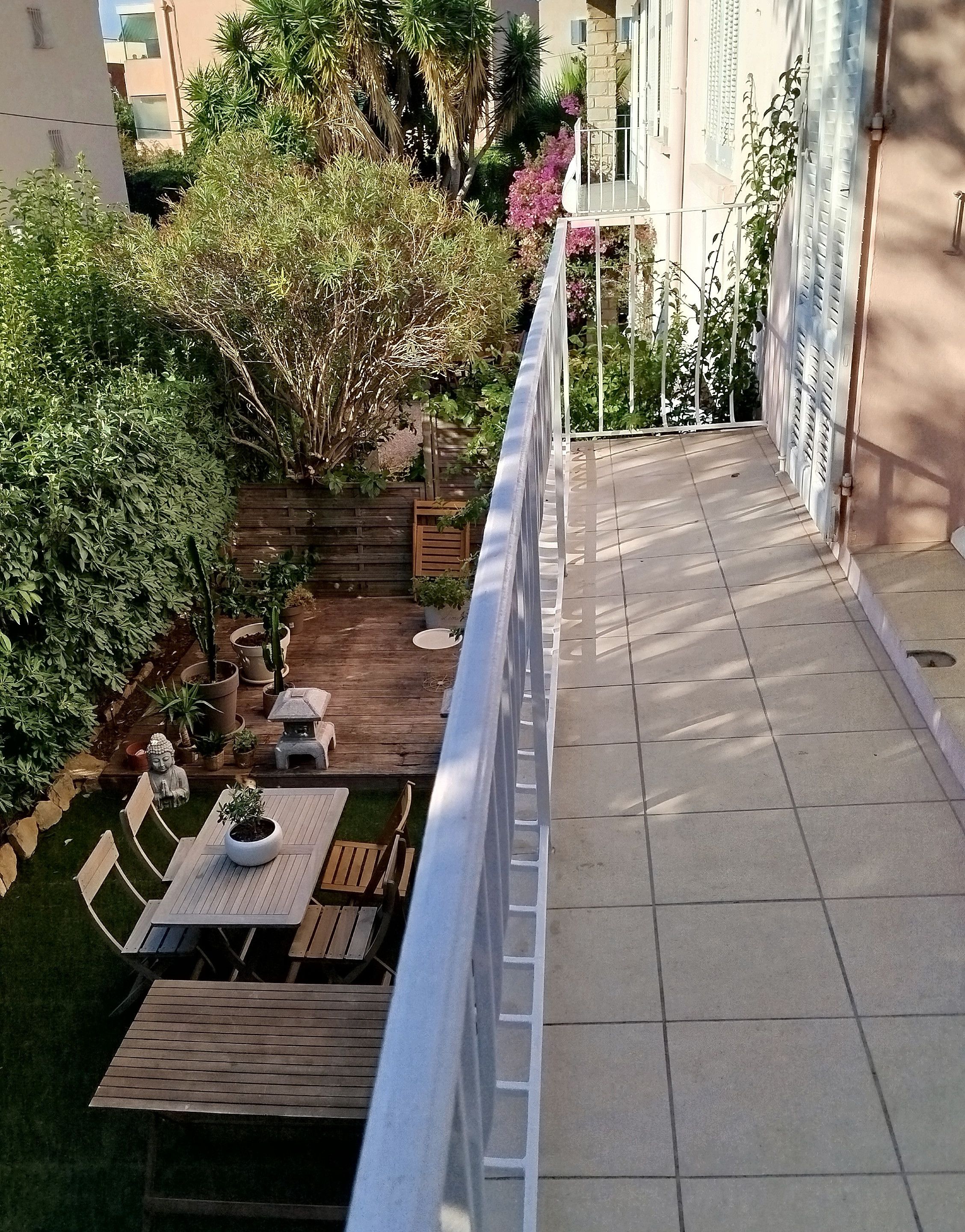 Ein Balkon mit Blick auf einen Garten, Gartenmöbel und eine Statue.