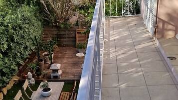A balcony with a view of a garden, outdoor furniture, and a statue.