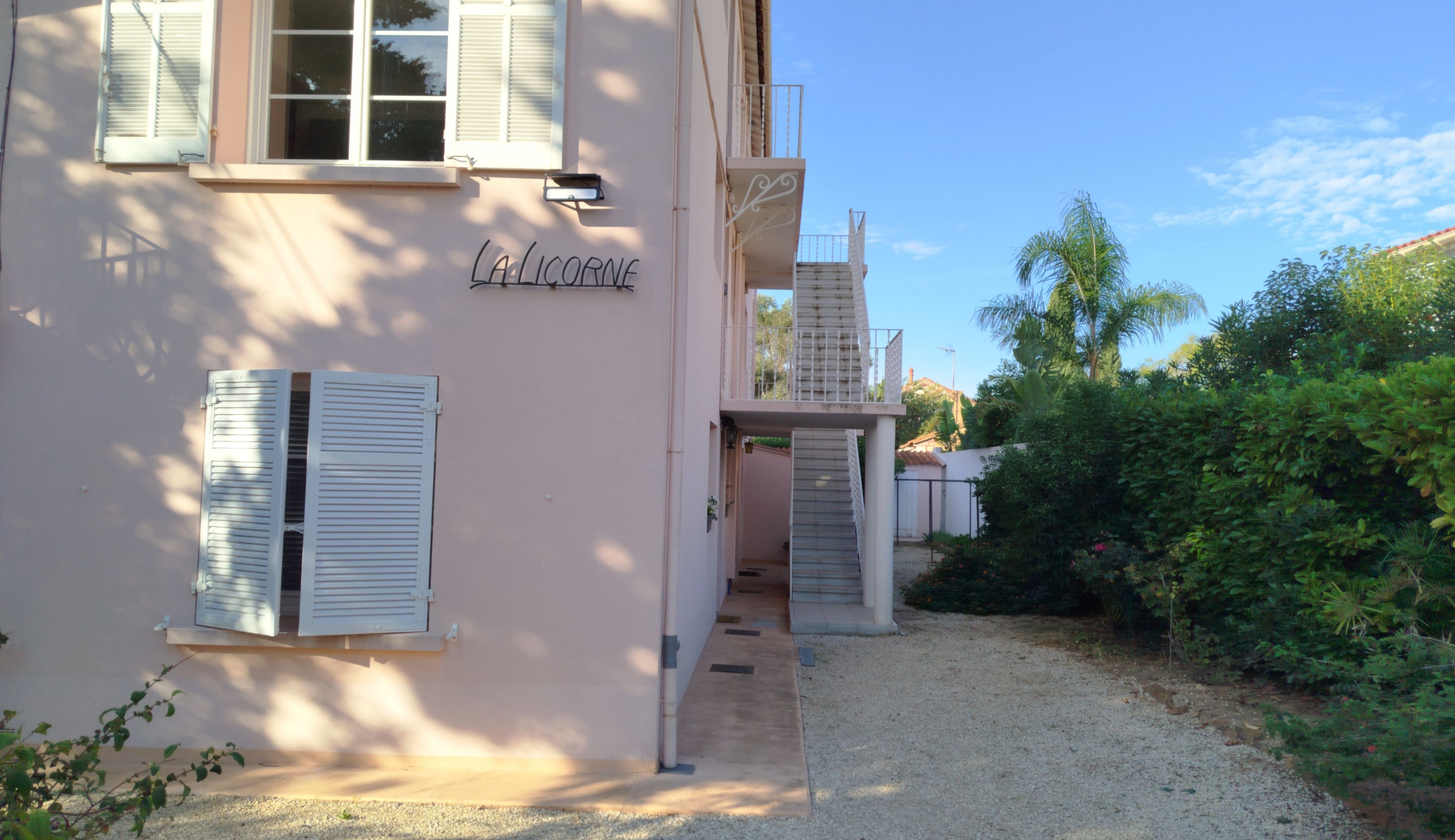 Ein Gebäude mit einem Namensschild, einem Balkon und einem Garten.