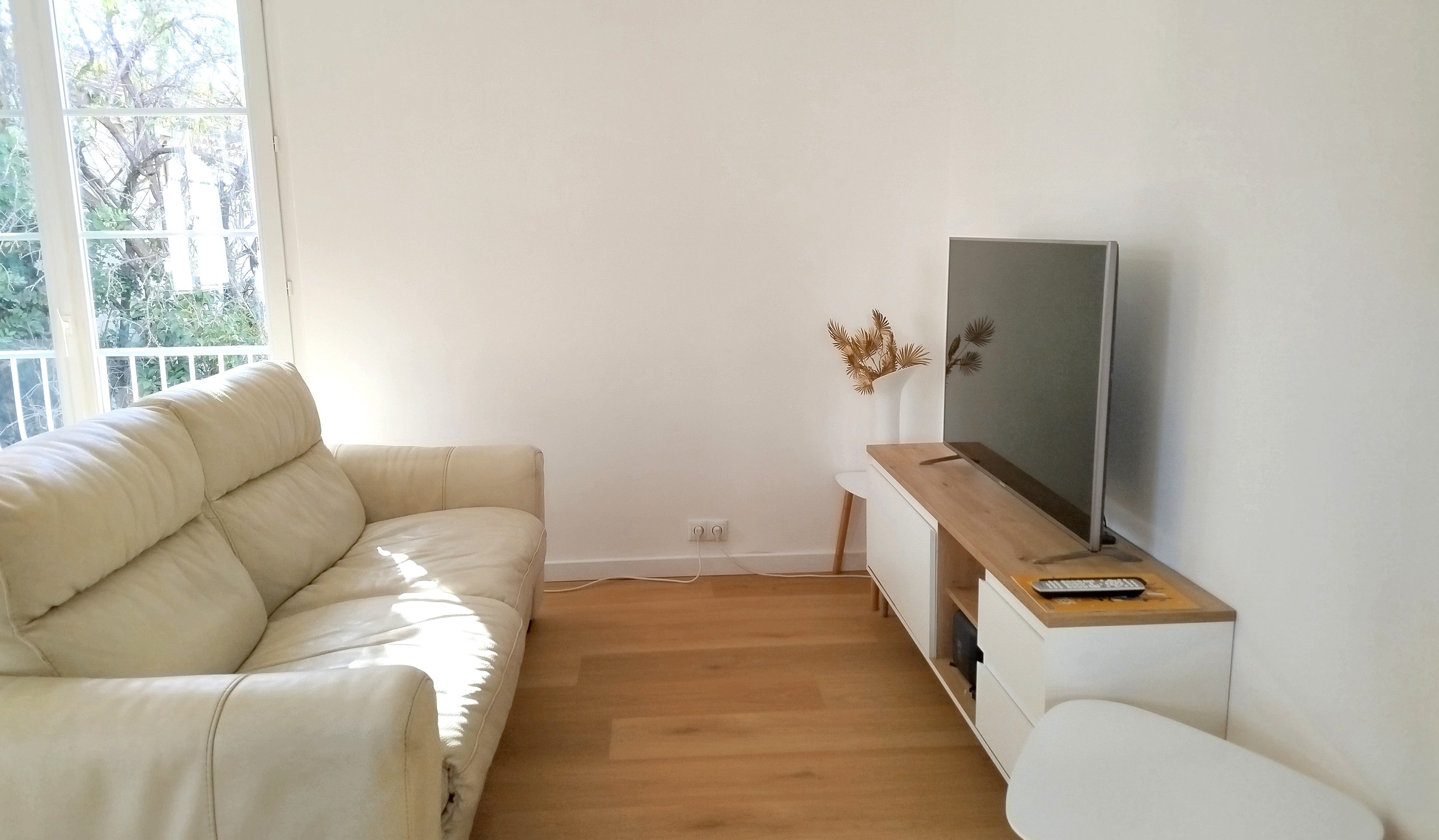 Un soggiorno con un divano bianco, un mobile TV in legno e una televisione a schermo piatto.