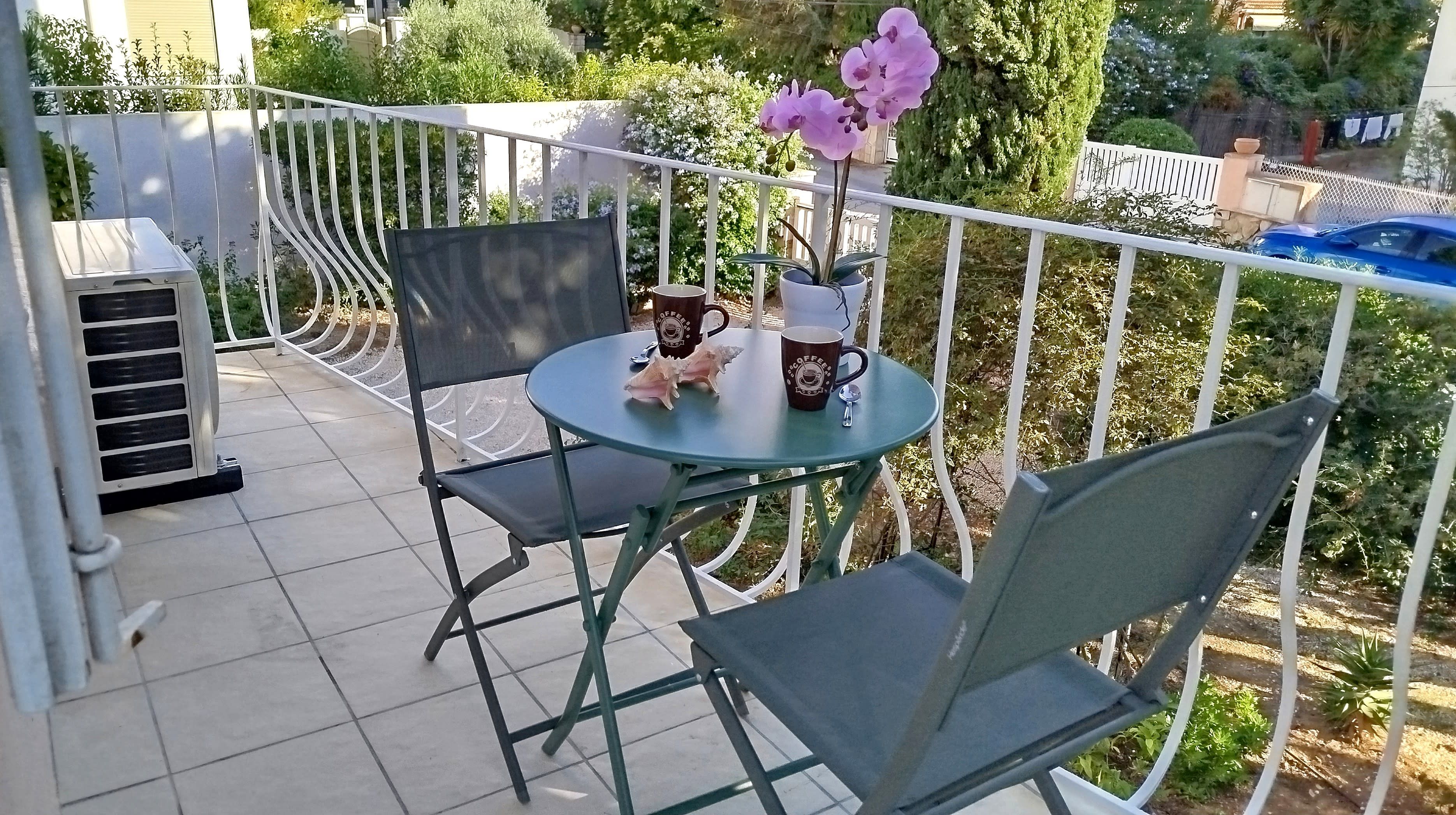 Ein Balkon mit Tisch, Stühlen, einer Kaffeetasse und einem Blumentopf.
