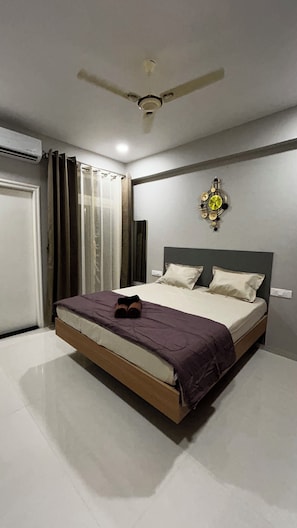 Ein Schlafzimmer mit einem Bett, einem Deckenventilator, einer Wanduhr und einem Fenster mit Vorhängen.