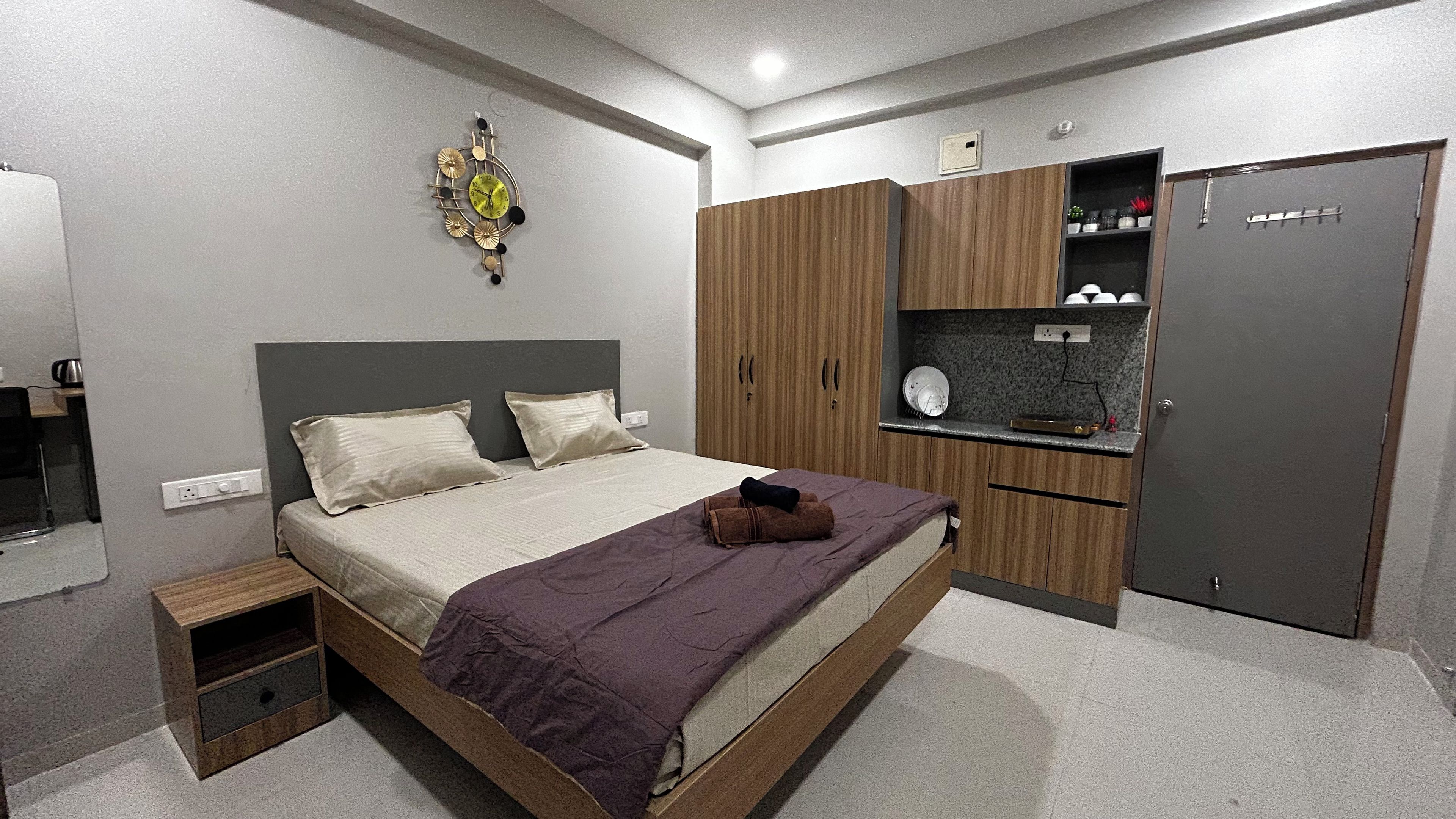 A bedroom with a bed, a wardrobe, a small table, and a wall clock.