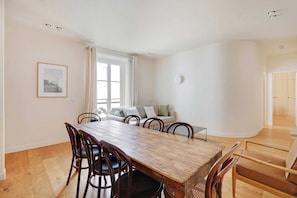 A dining area with a wooden table and chairs, a sofa, and a window with curtains. - Spacious Apartment 3br/8p - Opera (Paris)