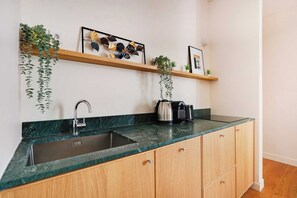 A kitchen with a sink, wooden cabinets, a marble countertop, and a coffee maker. - Spacious Apartment 3br/8p - Opera (Paris)