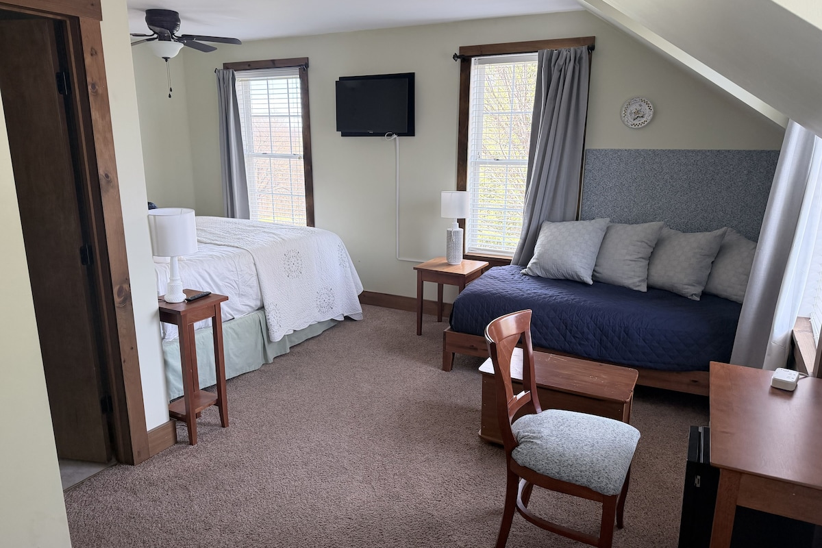 Ein Schlafzimmer mit Bett, Schreibtisch, Stuhl, Fernseher und Deckenventilator.
