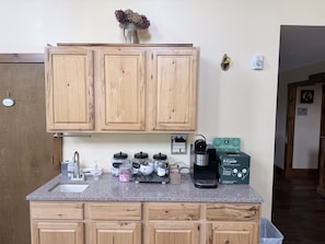Una cocina con armarios de madera, encimera de granito, cafetera y un cartel del programa de reciclaje.
