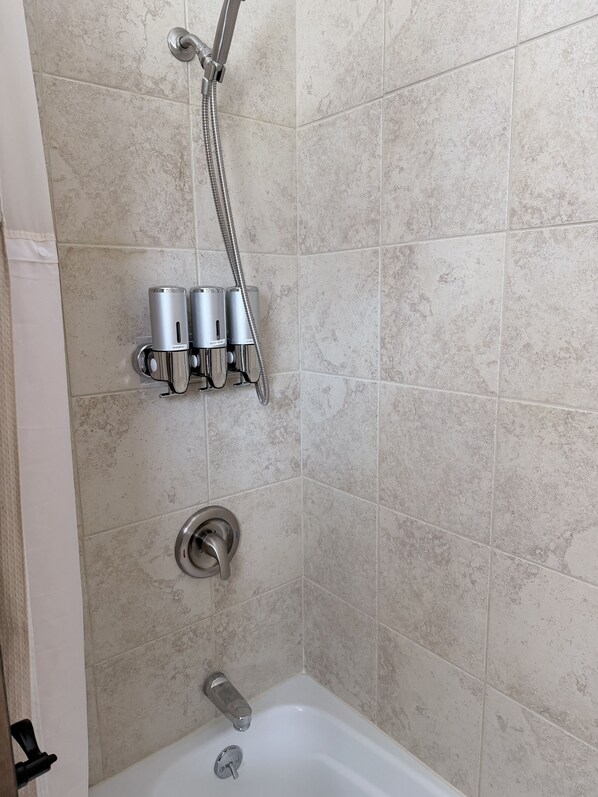 A shower area with a handheld showerhead, a wall-mounted faucet, and two soap dispensers. - Old Lantern Inn (Charlotte)