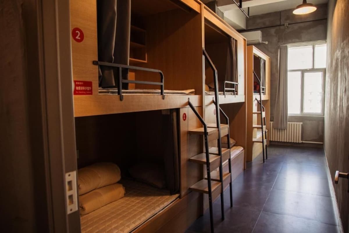 A dormitory room with bunk beds, a staircase, and a window providing natural light.